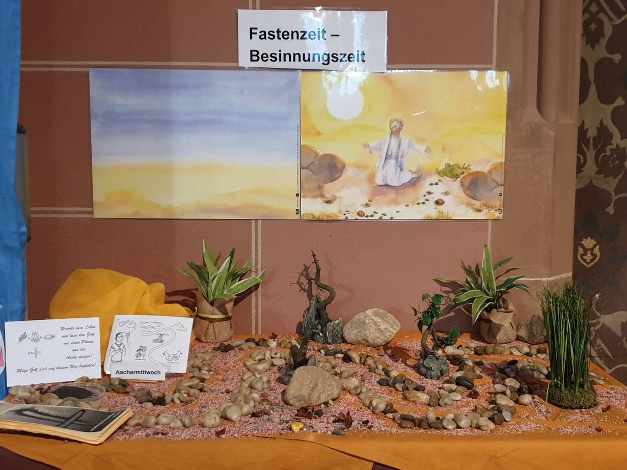Das Bild zeigt einen gestalteten Weg auf ockerfarbenen Tüchern. Im Hintergrund Bilder die Jesus in der Wüste zeigen.