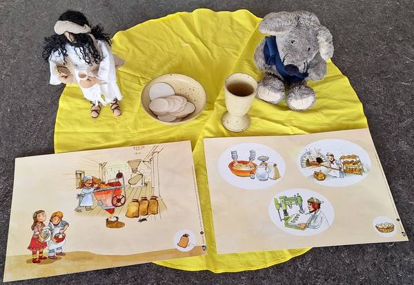 Das Bild zeigt eine Biblische Erzählfigur mit Kelch uns Brot, Jakobi die Münstermaus und Kamishibaibilder zur Entstehung von Hostien